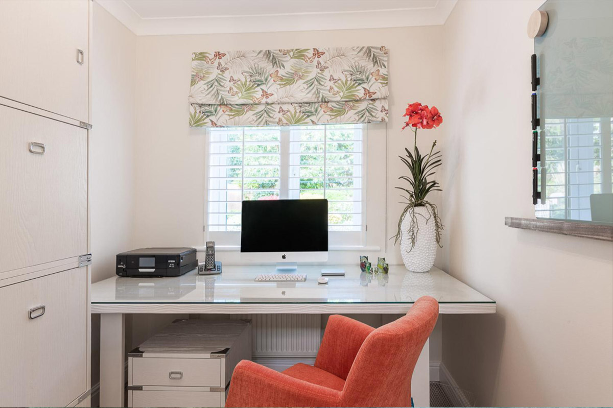 Home office with a glass-topped desk, botanical blind and coral chair