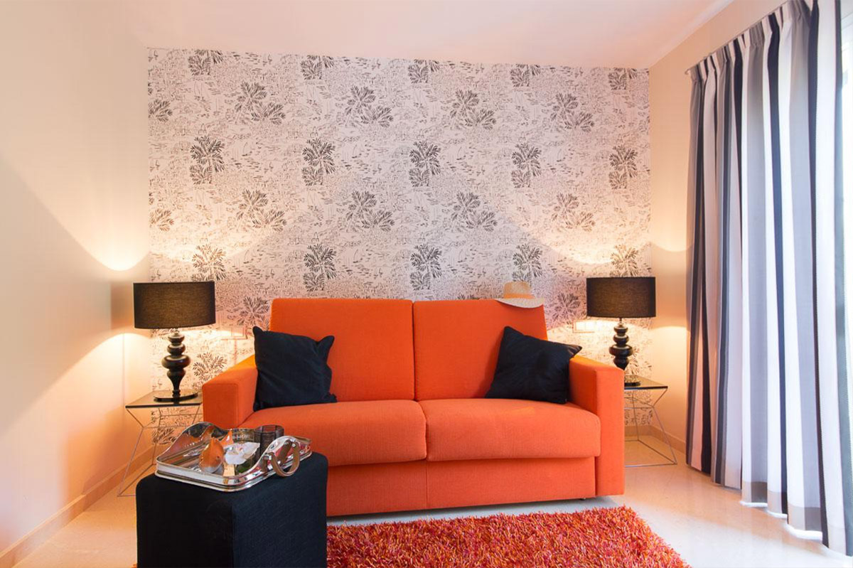 Cosy sitting room with an orange sofa, dark cushions and patterned feature wall