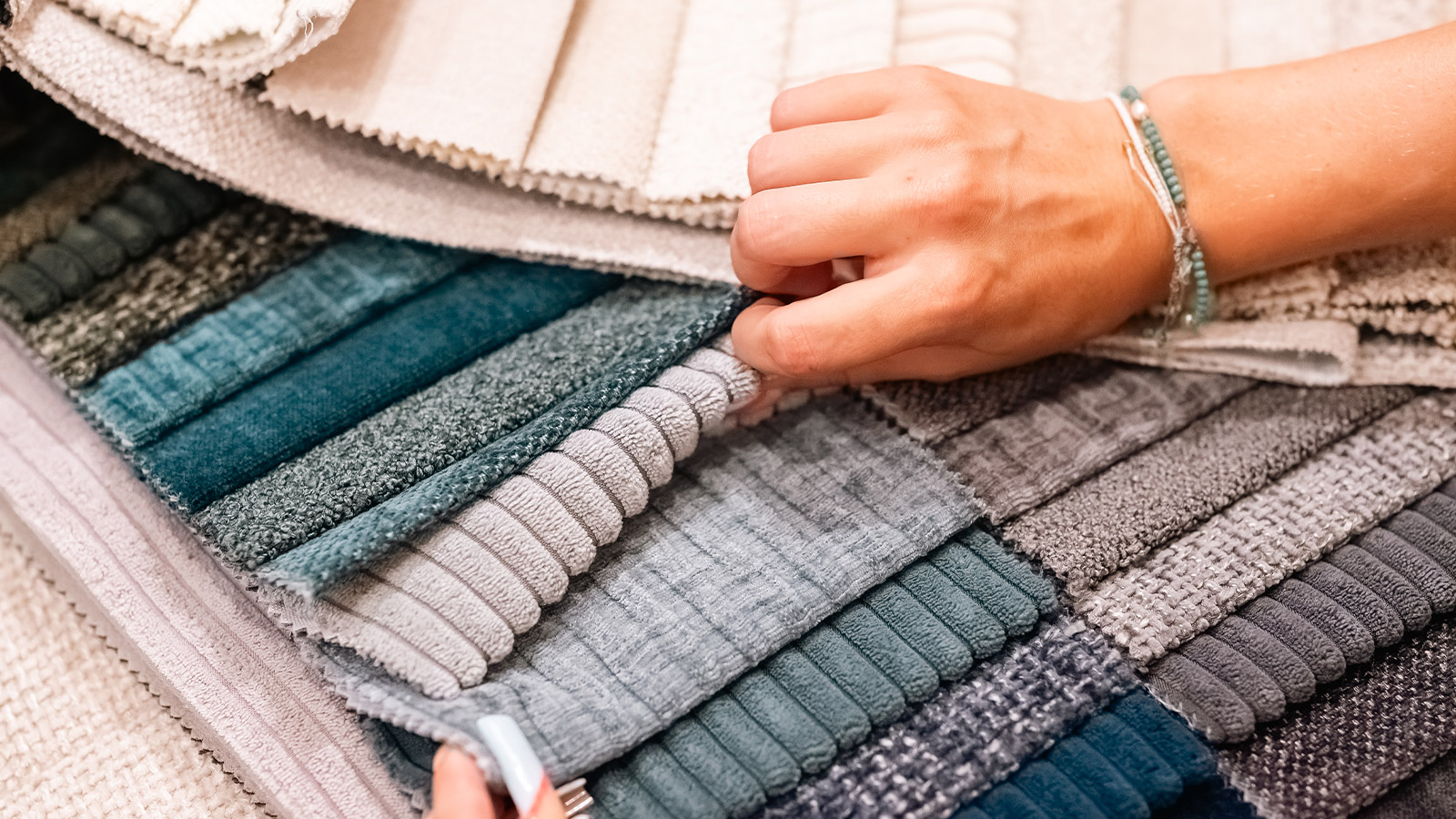 A hand feeling upholstery samples in cream, grey and teal